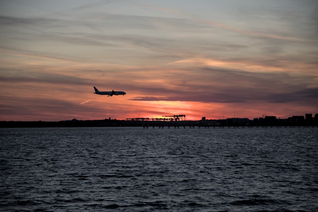 A plane flying over a body of water at sunset — Photo by Satish Dharmavarapu on Unsplash
